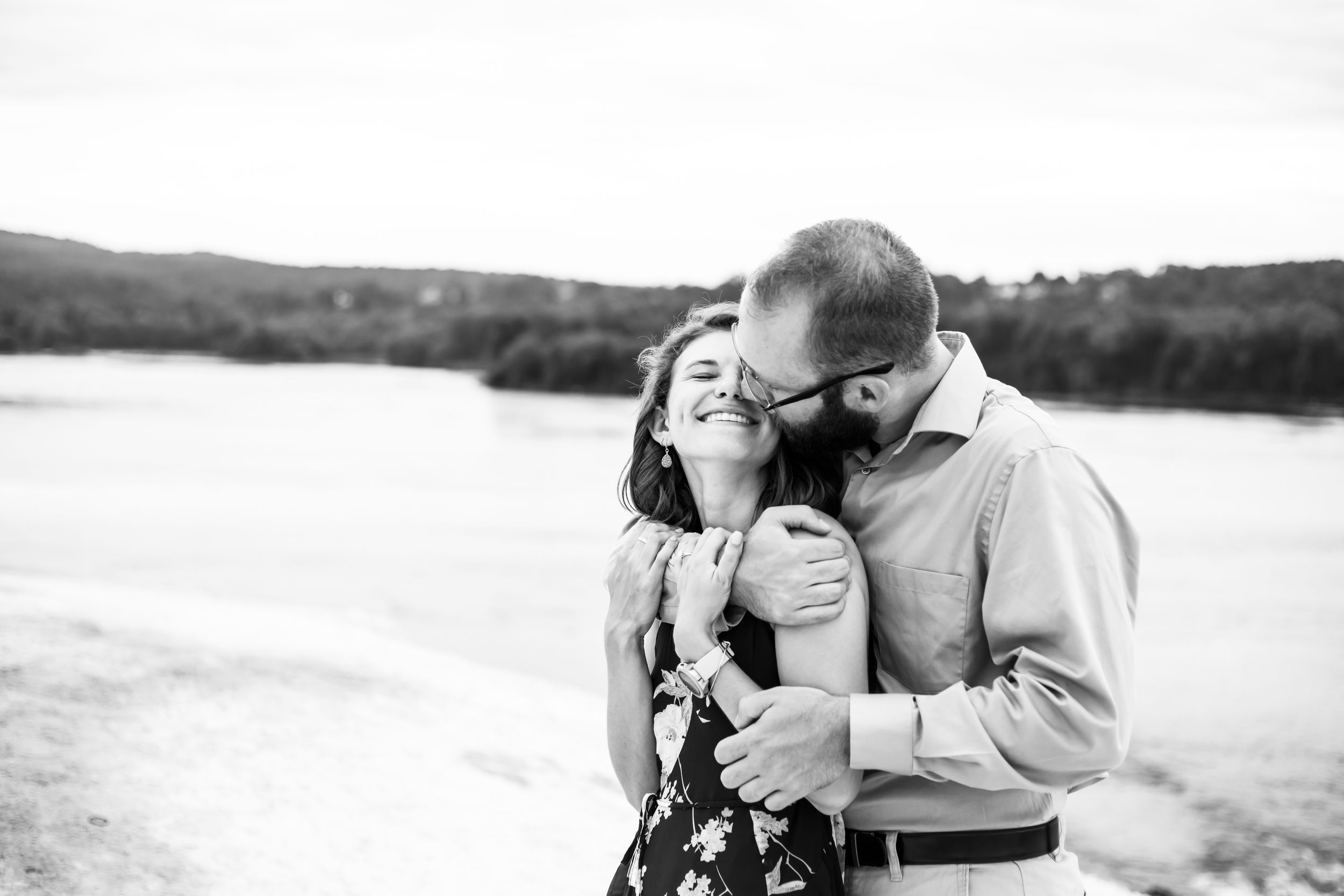 A romantic black and white moment captured between a couple embracing by a serene lakeside.