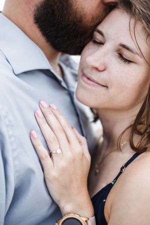 Close-up of a tender romantic moment showing hands with an engagement ring and delicate pink nail polish.