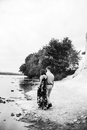 A couple walks along a scenic beach shoreline in black and white photography.