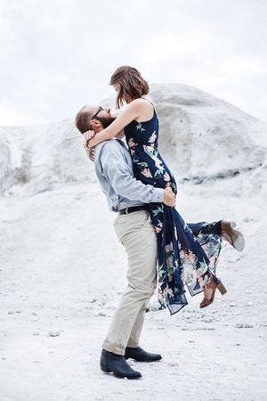 Playful couple embracing and spinning on a bright white rocky landscape.