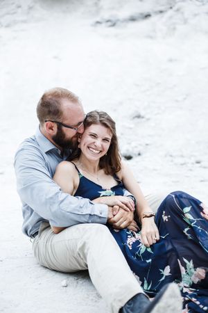 Intimate couple cuddling and laughing together on white rocks by the water.