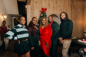 Group of five people posing together at a festive Christmas party with a decorated tree in the background.