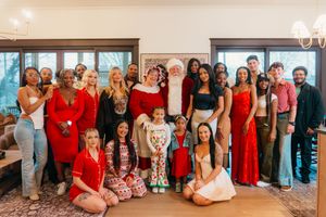 Large festive group photo with Santa Claus, adults and children wearing holiday outfits in a decorated indoor setting.
