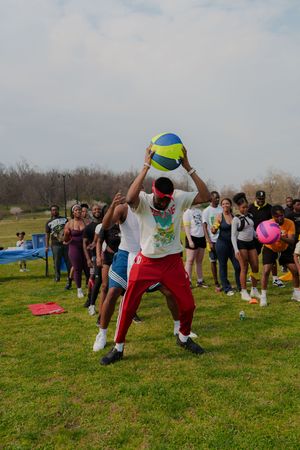 Group of people playing with a volleyball outdoors on a grass field during a casual sports gathering on a cloudy day.