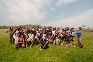 Large diverse group of people posing together outdoors on a green field under a partly cloudy sky.