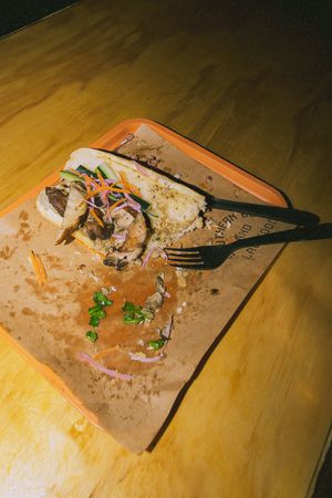 Messy food tray with leftover sandwich, fresh herbs, pickled onions, and a black plastic fork on parchment paper.