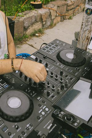 DJ mixing music outdoors on a Pioneer DJ controller, hands adjusting knobs at an open-air event.