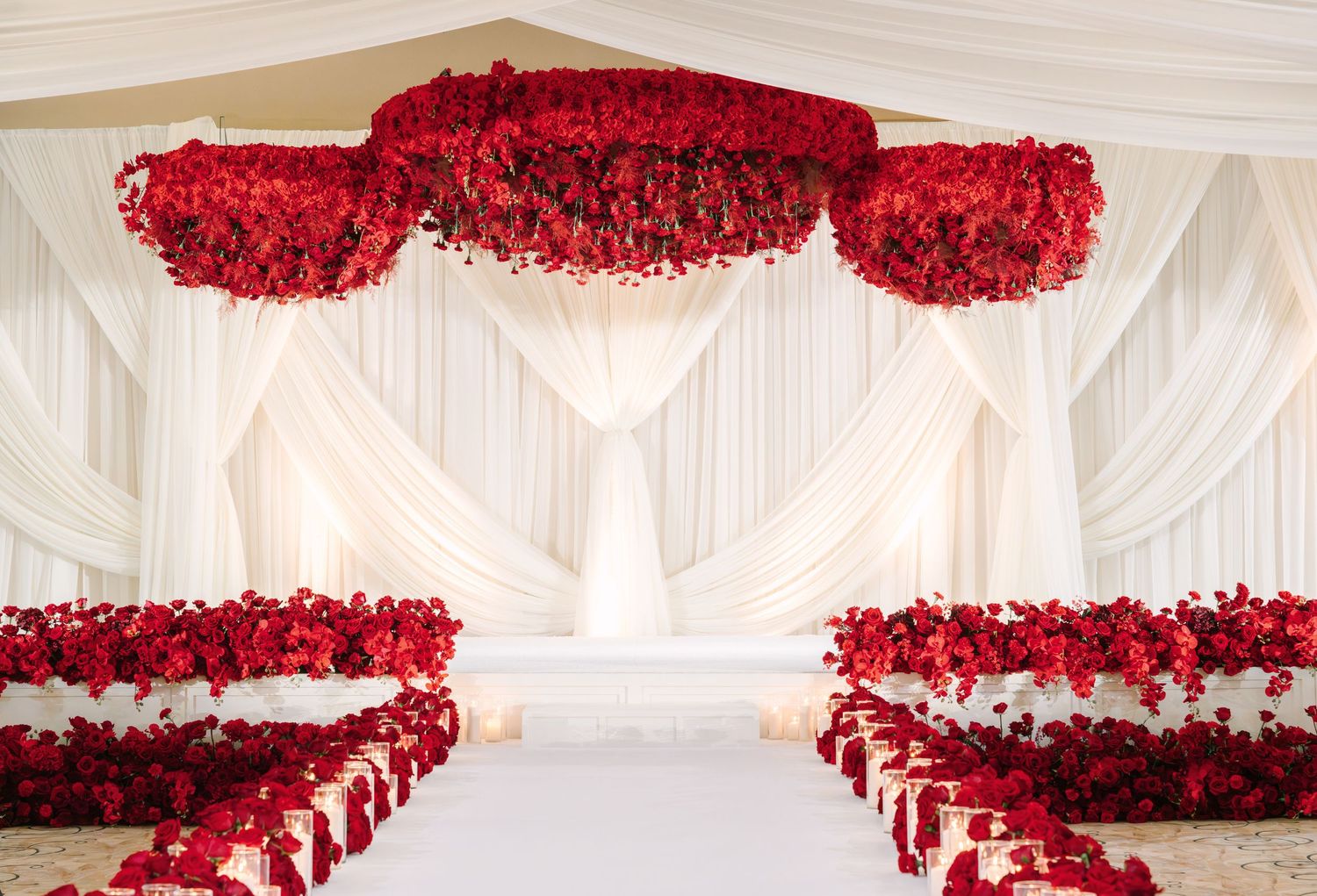 Lush red rose and orchid floral wall display with glowing white pillar candles at an elegant wedding reception.