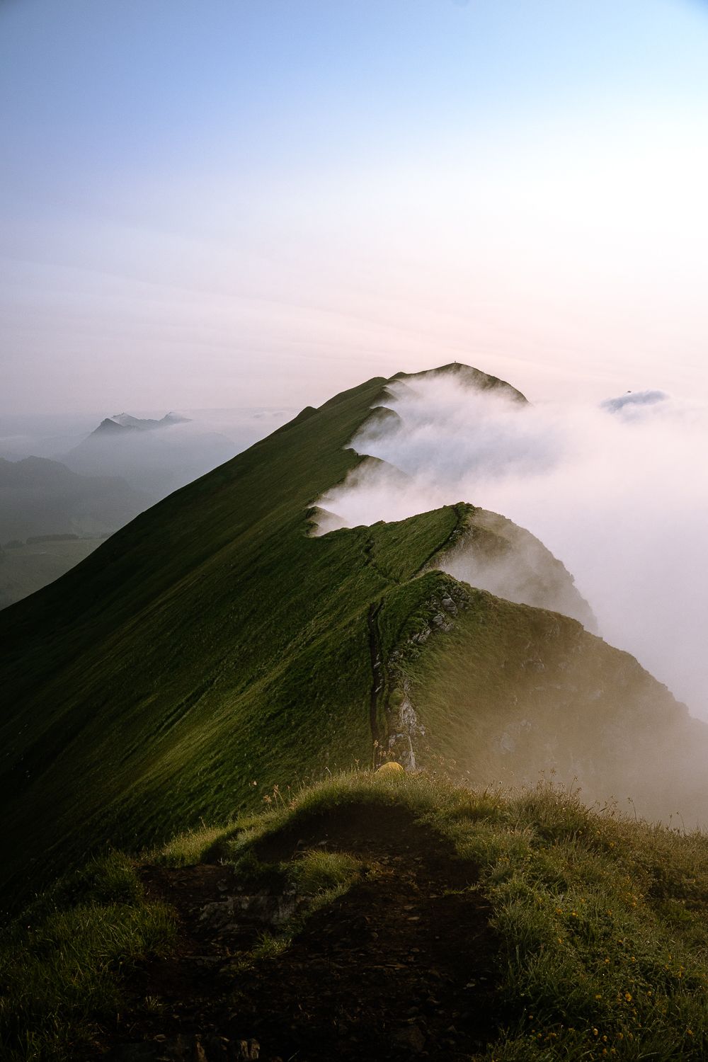 Blick auf den schmalen Grat des Augstmatthorns, während dichte Nebelschwaden im sanften Morgenlicht über die grünen Berghänge ziehen.