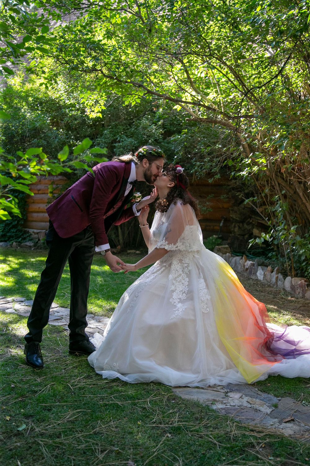 A romantic wedding couple in burgundy and white attire share intimate moments in a lush garden setting.