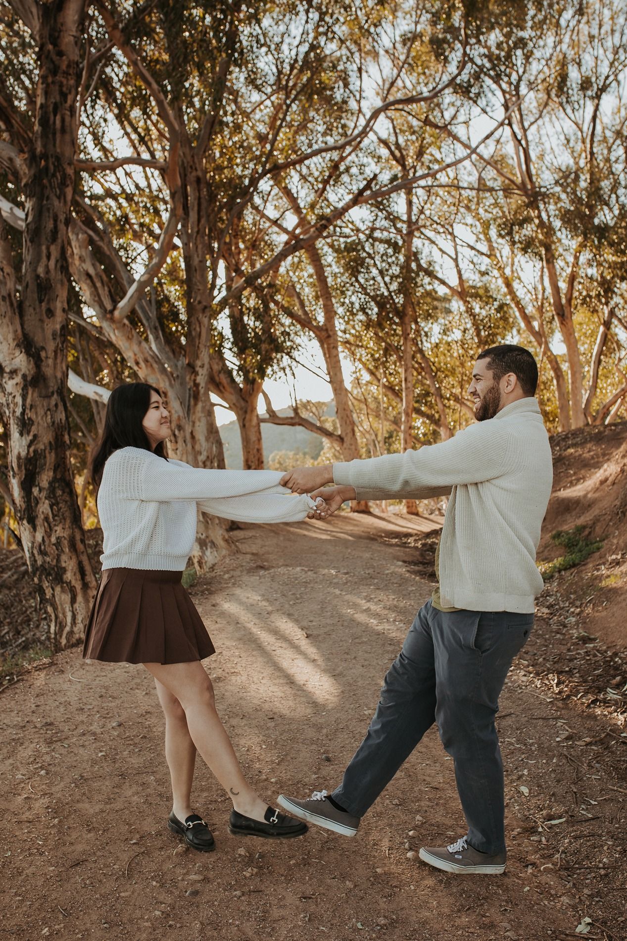 A couple dances playfully on a dirt path surrounded by eucalyptus trees during golden hour at Will Rogers State Park.