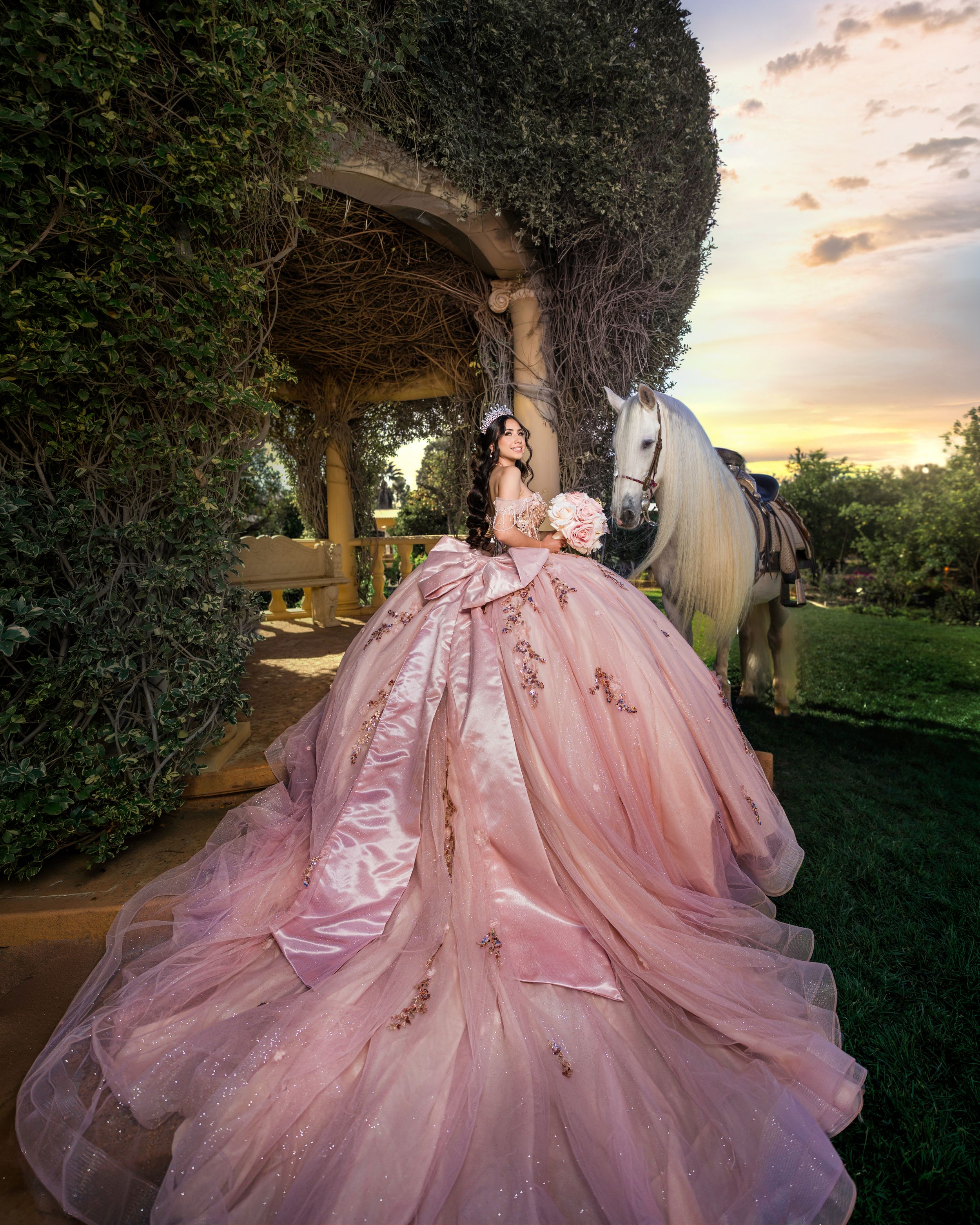 A flowing pink ball gown with intricate details photographed in a garden setting during golden hour sunset.