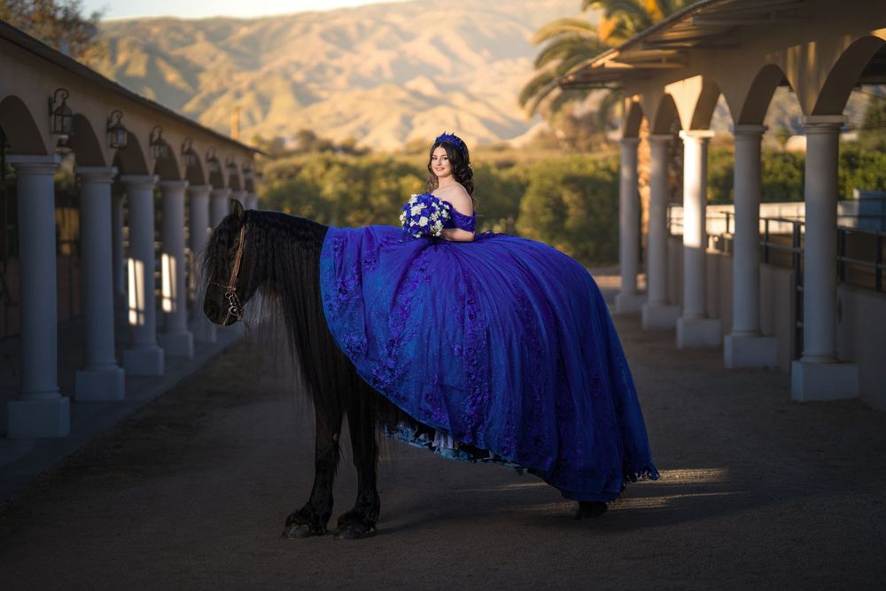A flowing blue dress creates a dramatic silhouette against arched stone columns at sunset.