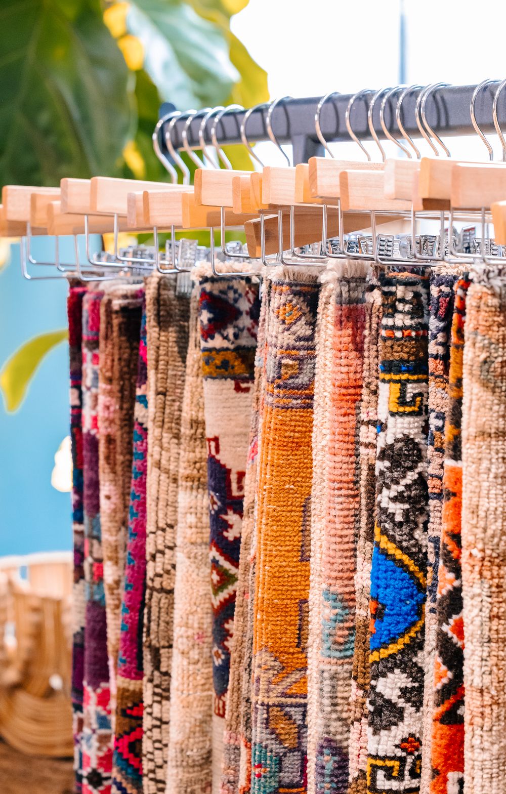 Colorful handwoven Persian rugs displayed on wooden hangers at an outdoor market.