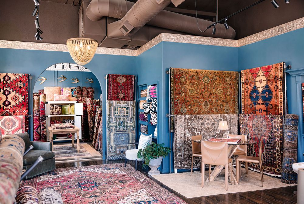 Colorful Persian and Oriental rugs displayed on blue walls in a decorative rug showroom with chandelier lighting.