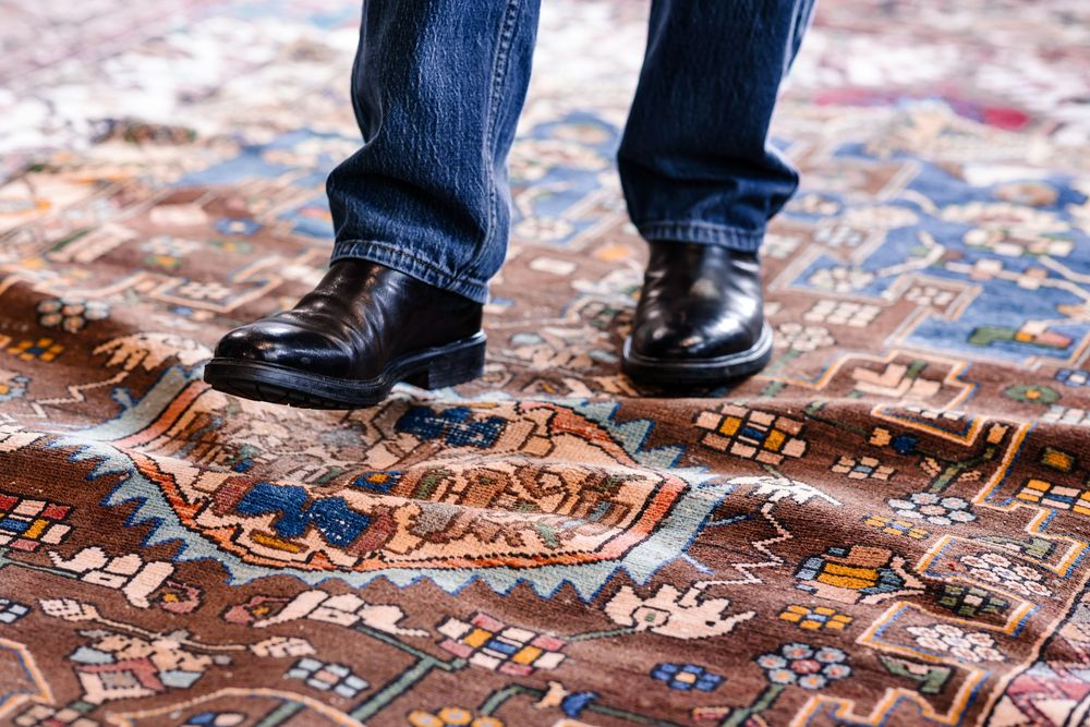 Person wearing black leather dress shoes and jeans standing on a decorative vintage Persian area rug.