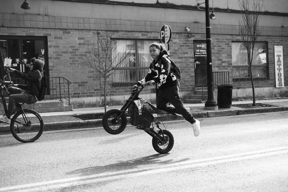 Person performing a wheelie on an electric scooter on a city street in black and white photo.