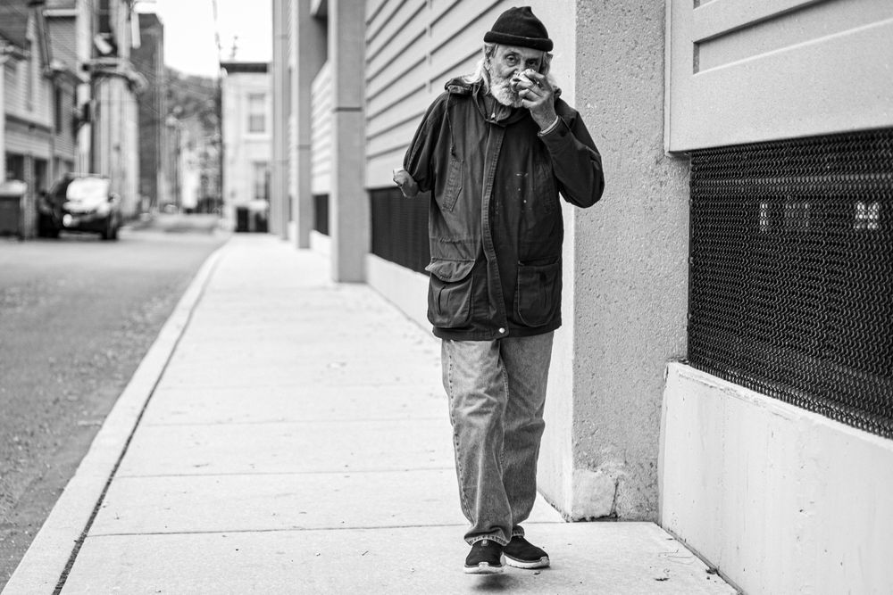 Black and white photo of a man in a dark jacket walking on a city sidewalk while talking on a phone.
