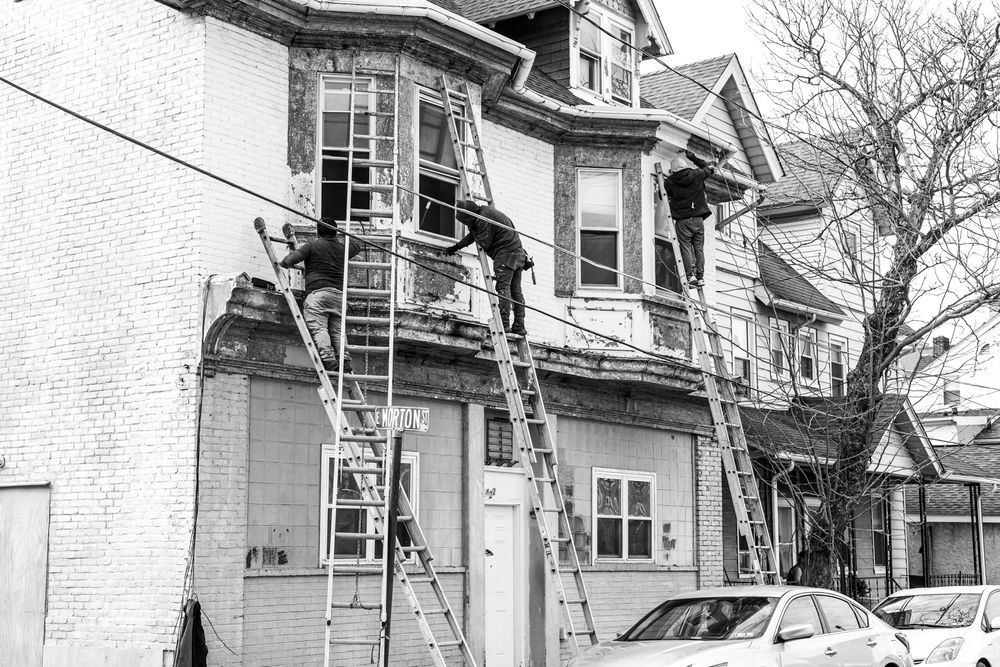 Workers on ladders renovating the exterior of a multi-story brick building in black and white photo.