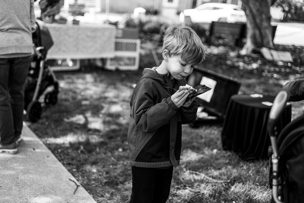 Black and white photo of a young boy examining a small object outdoors at a community event.