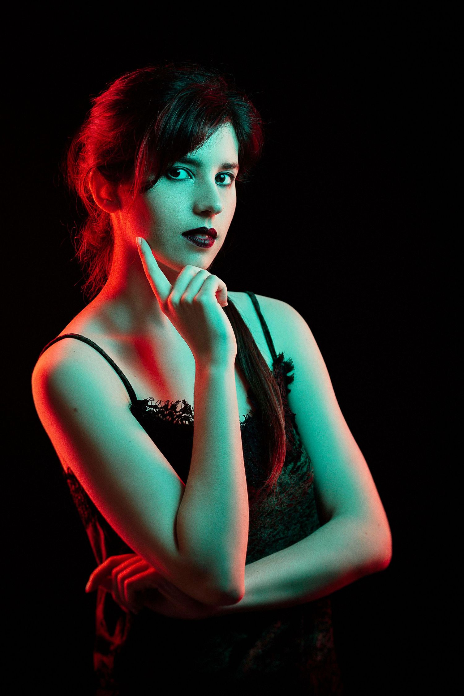 Young woman with dark hair posed dramatically under red and green neon lights against a black background.