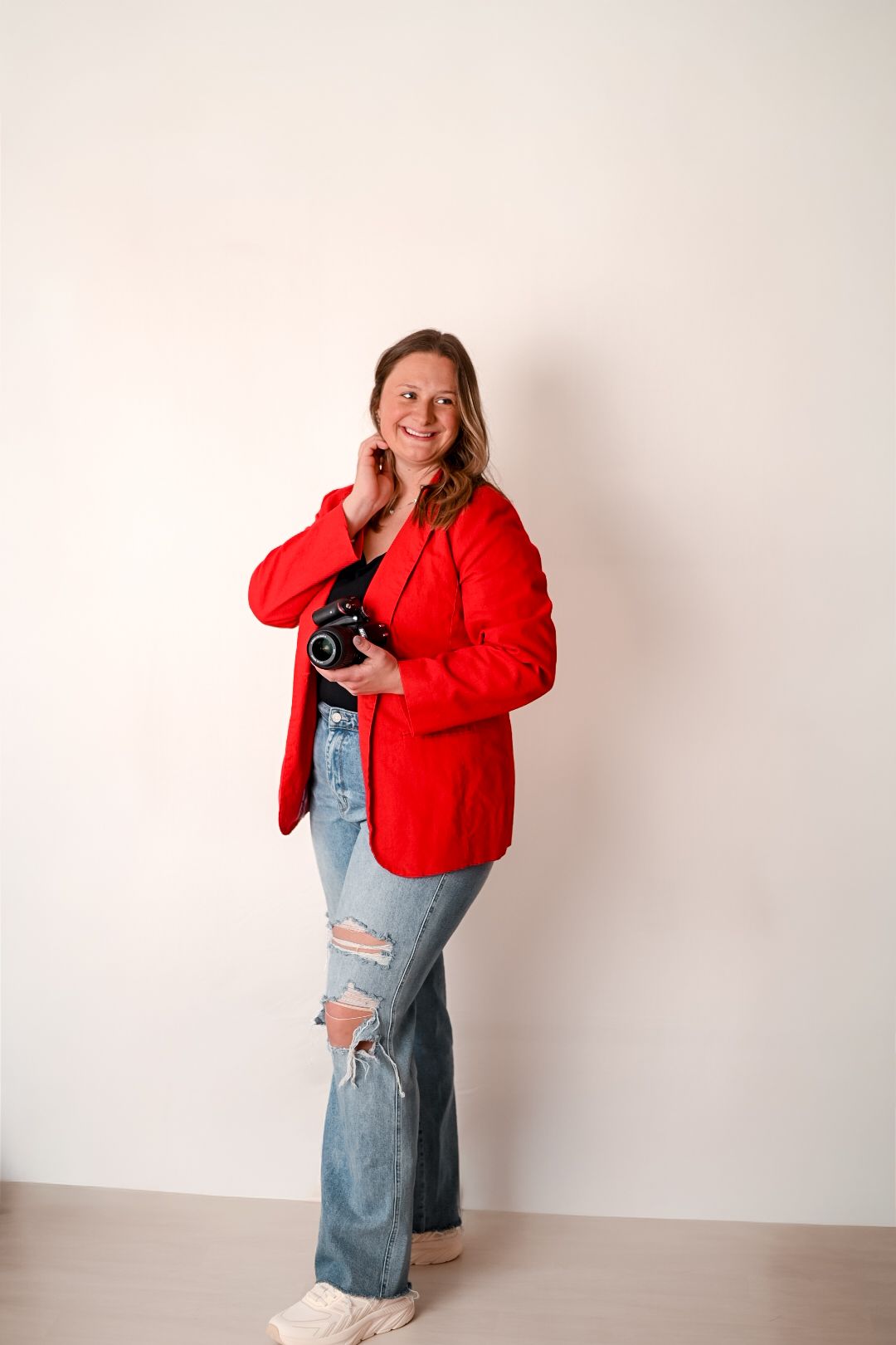 A person wearing a bright red jacket and denim overalls poses playfully against a white wall in four different poses.