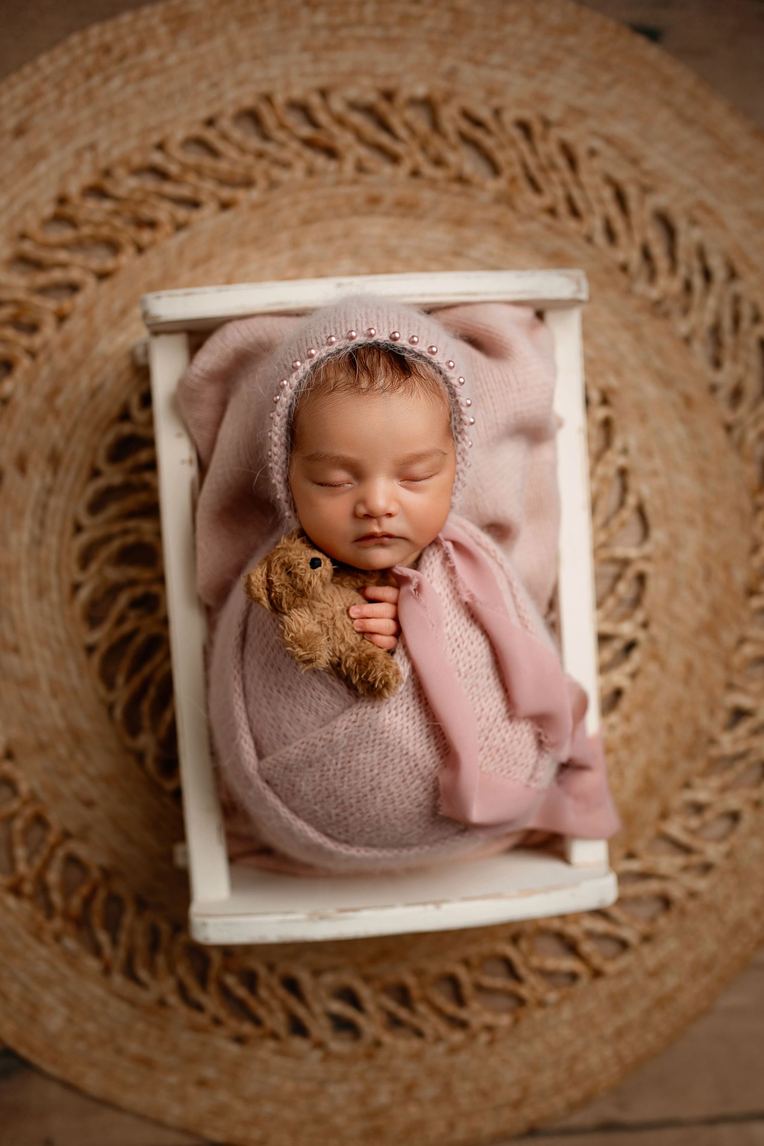Newborn baby girl wrapped in pink with bonnet and teddy bear in white cradle bed at Flowertown Photography Studio in Summerville, SC