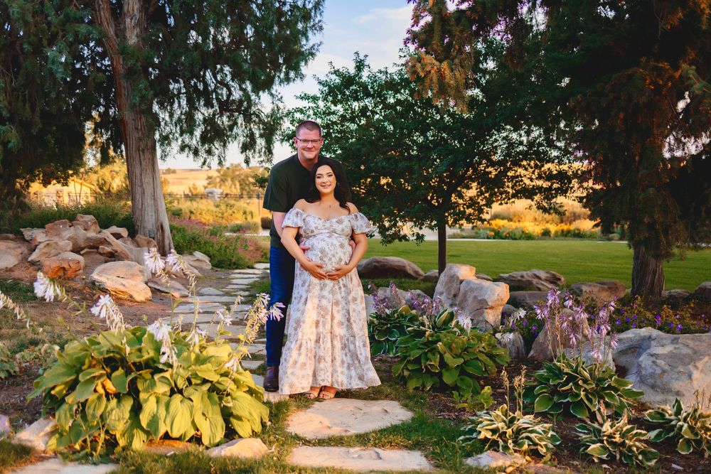 Romantic sunset photo session in a lush garden setting with stone pathways and autumn foliage.  A pregnant woman stood in front of a man.