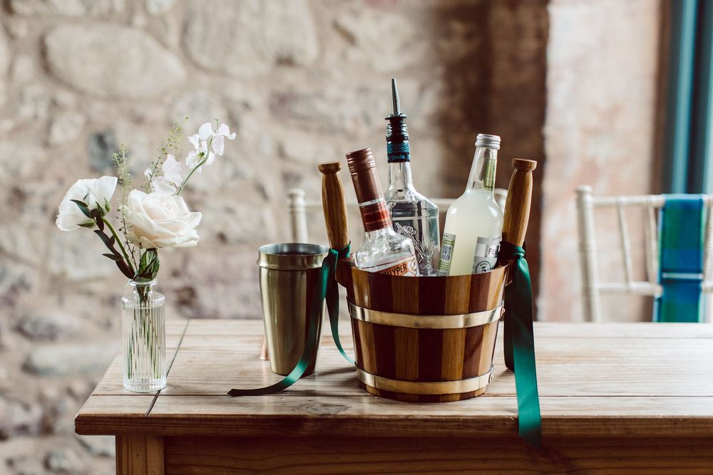 Elegant table settings with wine buckets and delicate flower arrangements line a rustic stone wall at a wedding venue.