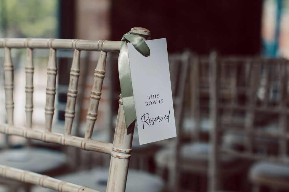 A white reserved seating card hangs from a light wooden chiavari chair at an event venue.