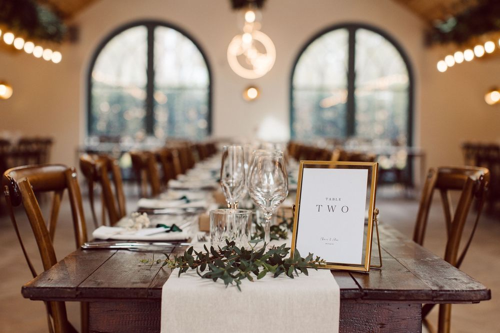 A rustic wedding reception venue with wooden tables, string lights, and greenery decorations creates an elegant atmosphere.