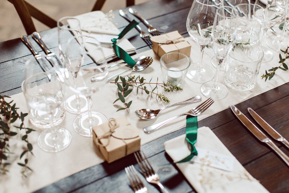 Elegant table setting with wine glasses, green bottles, and eucalyptus branches on a white linen tablecloth.
