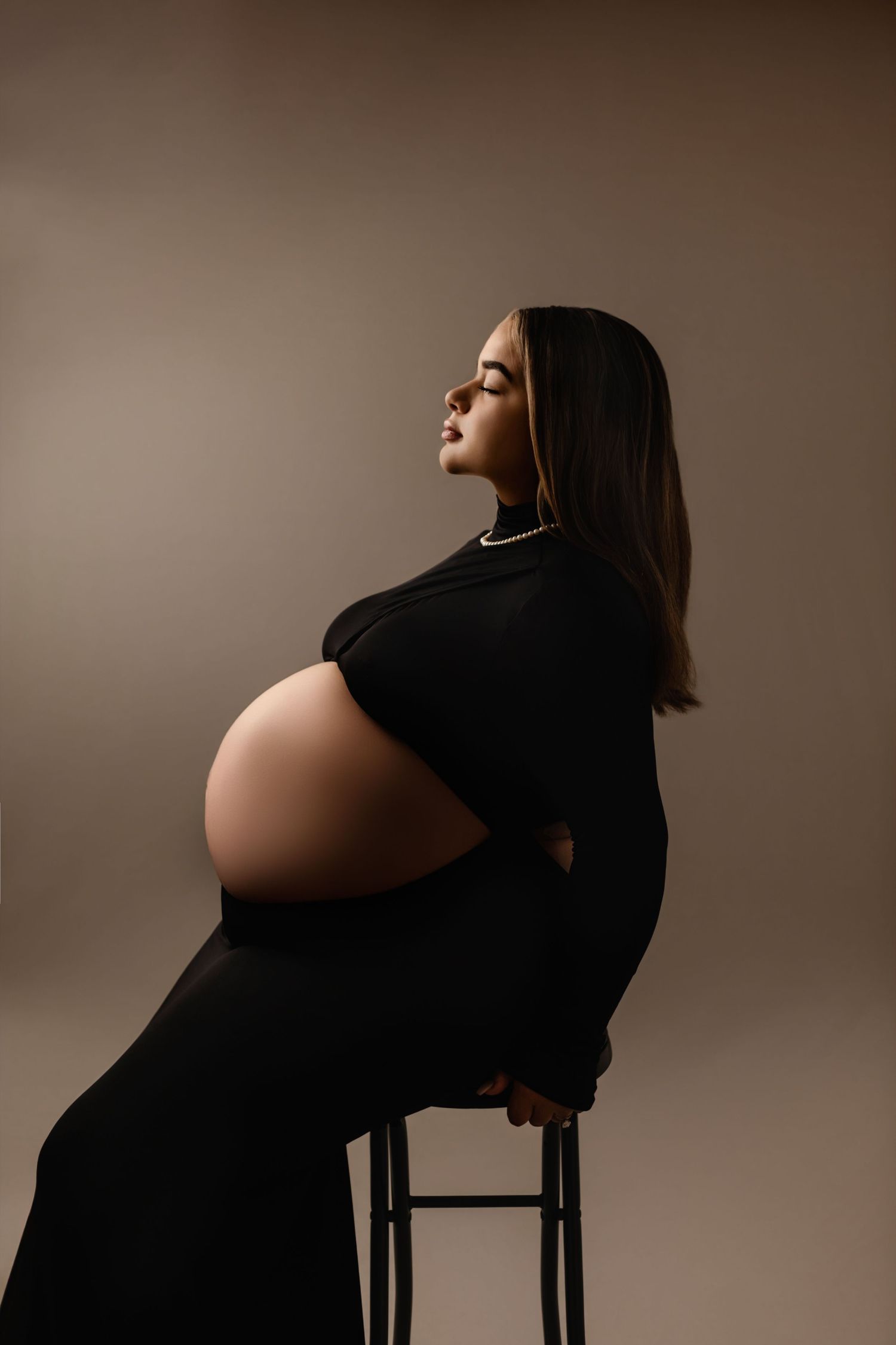 Pregnant mama sits on a bench enjoying a quiet moment in a sleek black dress, captured by Charlottesville maternity and baby photographer.
