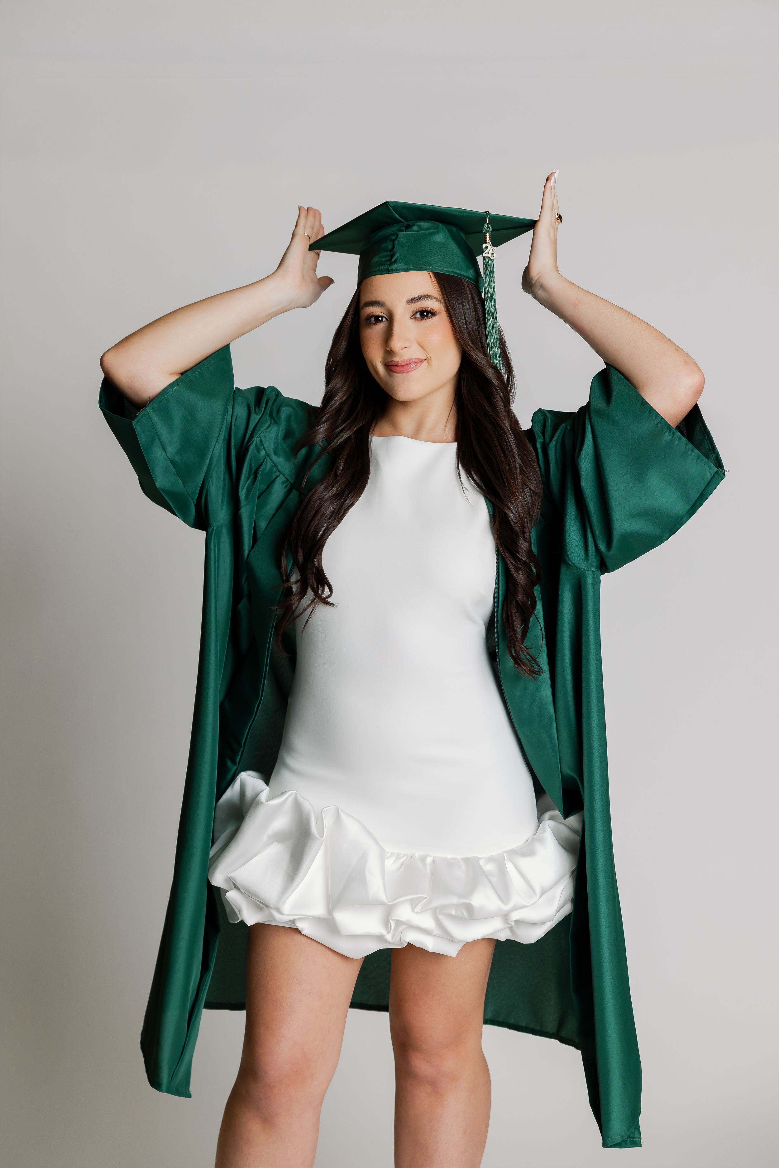 A woman in a green graduation gown stands against a plain background.