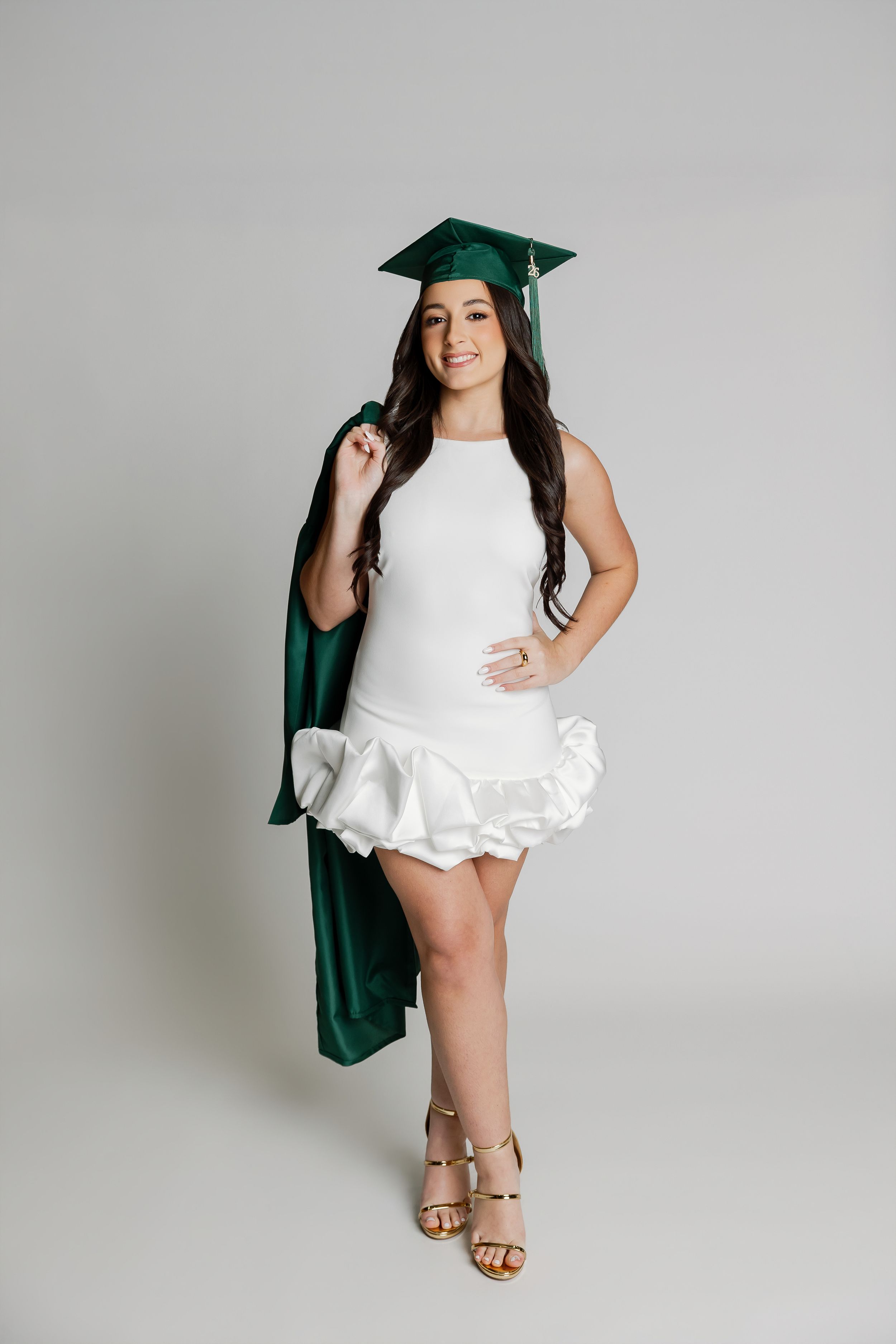 A smiling woman in a graduation cap and gown standing against a plain background.