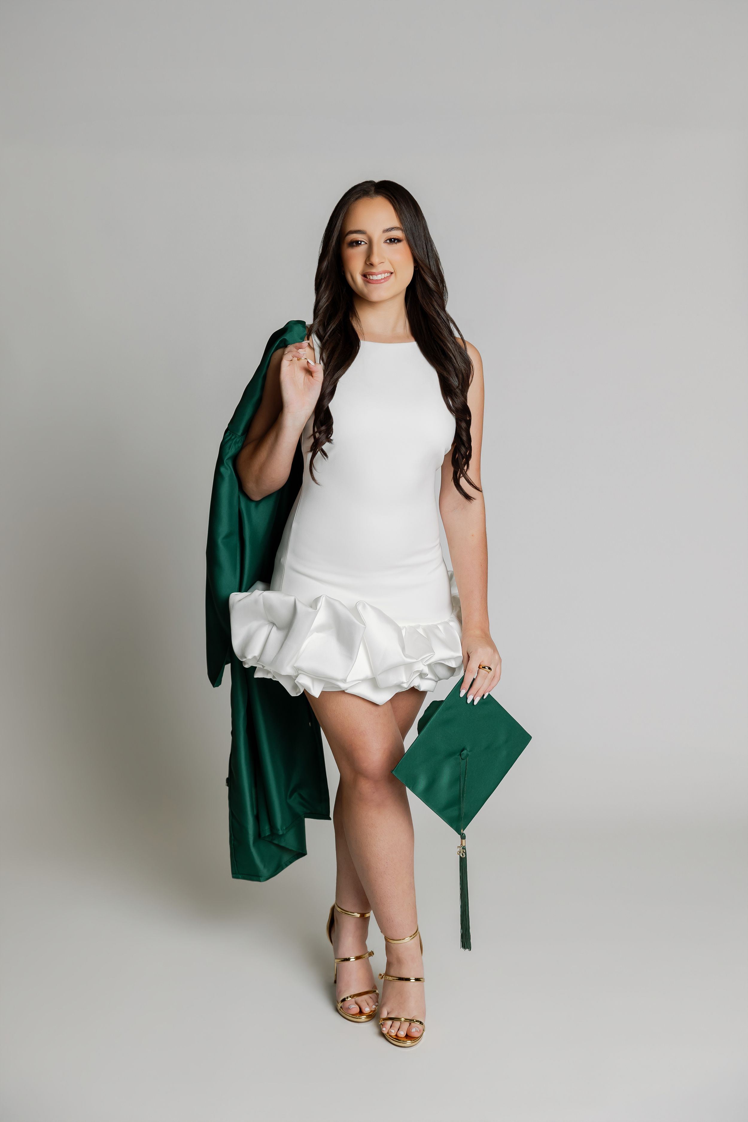 A woman in a green graduation gown stands against a plain background.