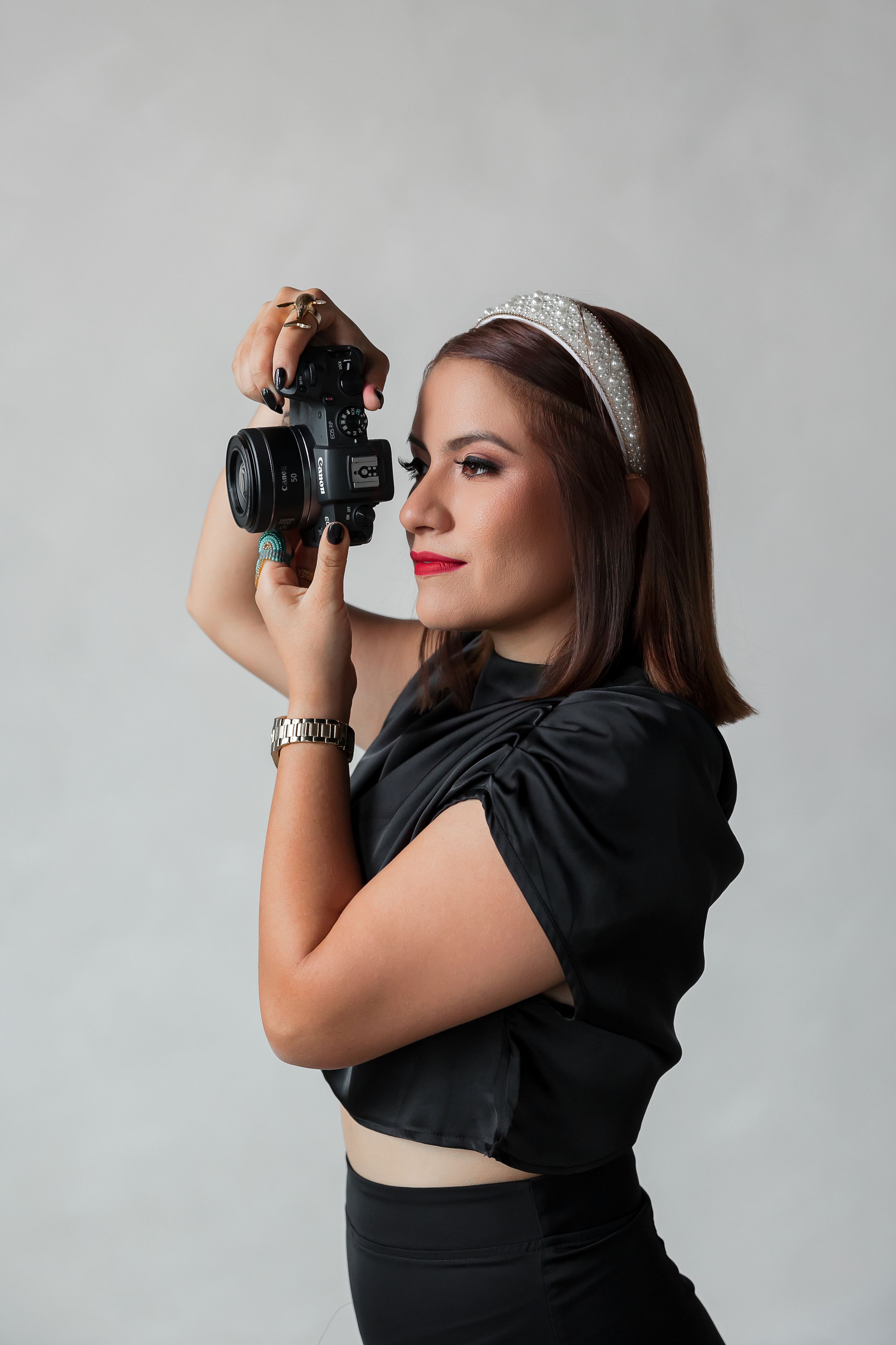 A young woman in a black outfit holding a camera and posing for a photo.