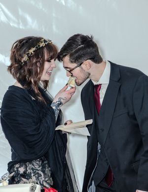 Couple sharing an intimate moment at wedding ceremony, bride in floral crown feeds groom cake.