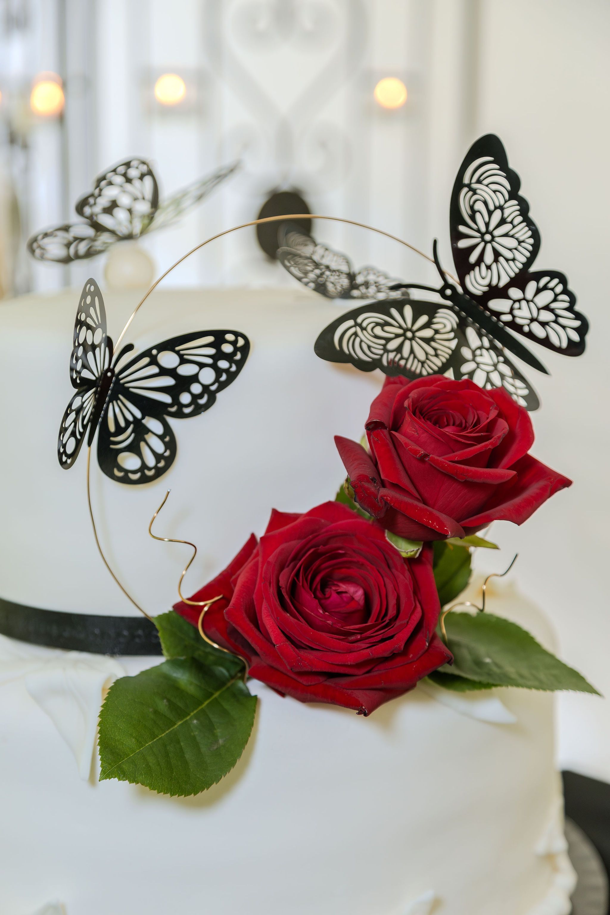 Elegant white wedding cake topped with black butterfly decorations and two red roses on a gold hoop.