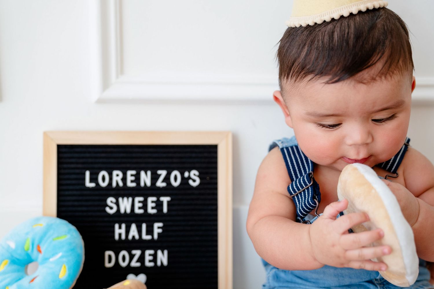 Baby in striped outfit lies on stomach with half-year milestone birthday cake in professional photo session series.