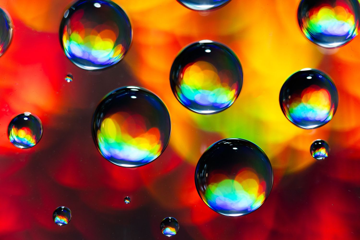 Colorful water droplets reflect rainbow prisms against a vibrant red and orange background creating an abstract macro pattern.