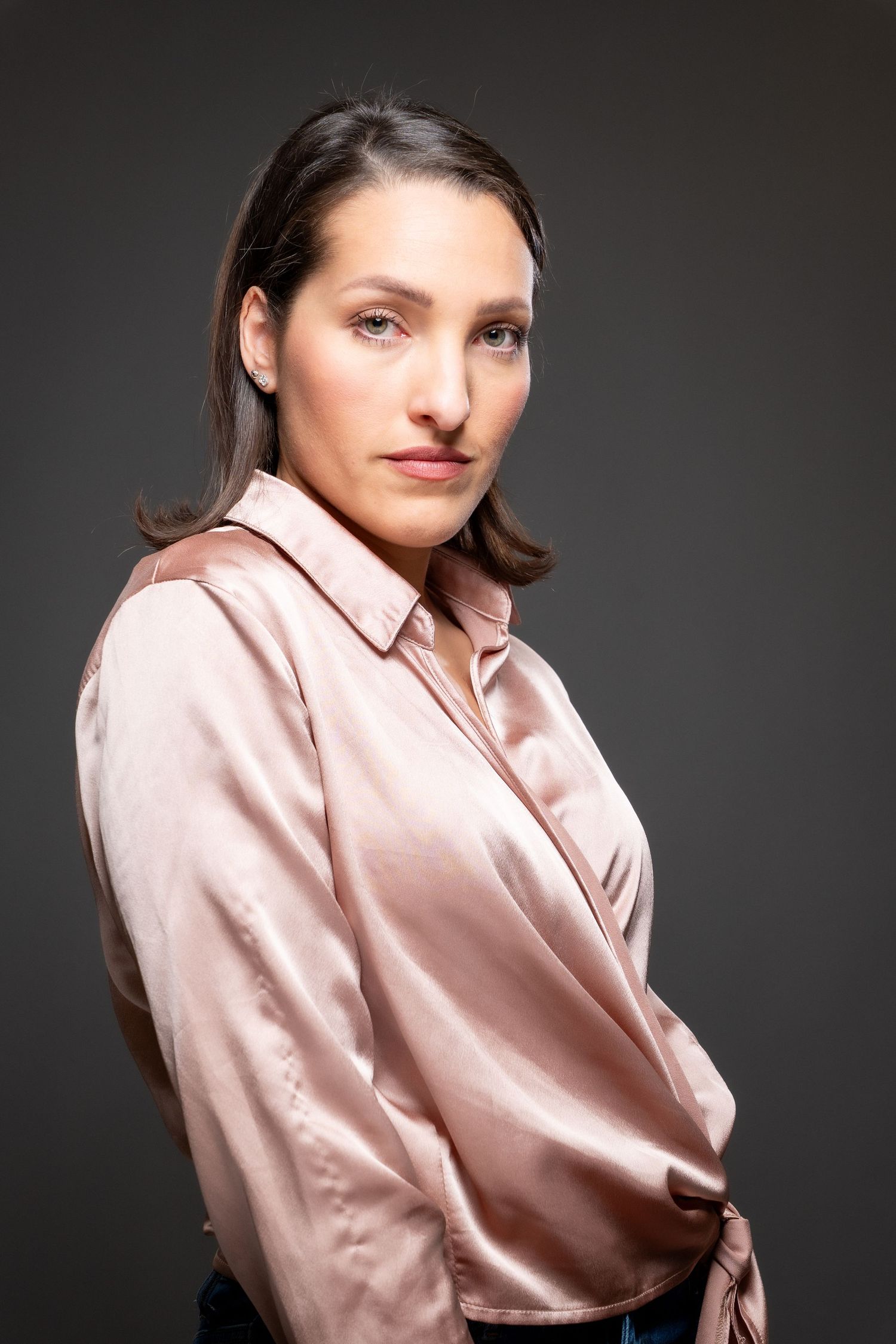 Fashion portrait series featuring a rose gold silk wrap blouse paired with dark denim in dramatic lighting.