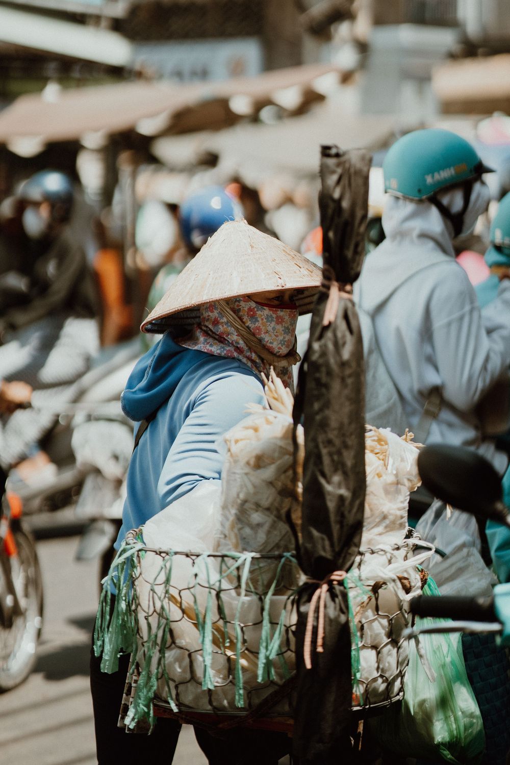 Vendeur de rue vietnamien portant un chapeau conique traditionnel et un masque facial transportant un panier de marchandises dans un marché