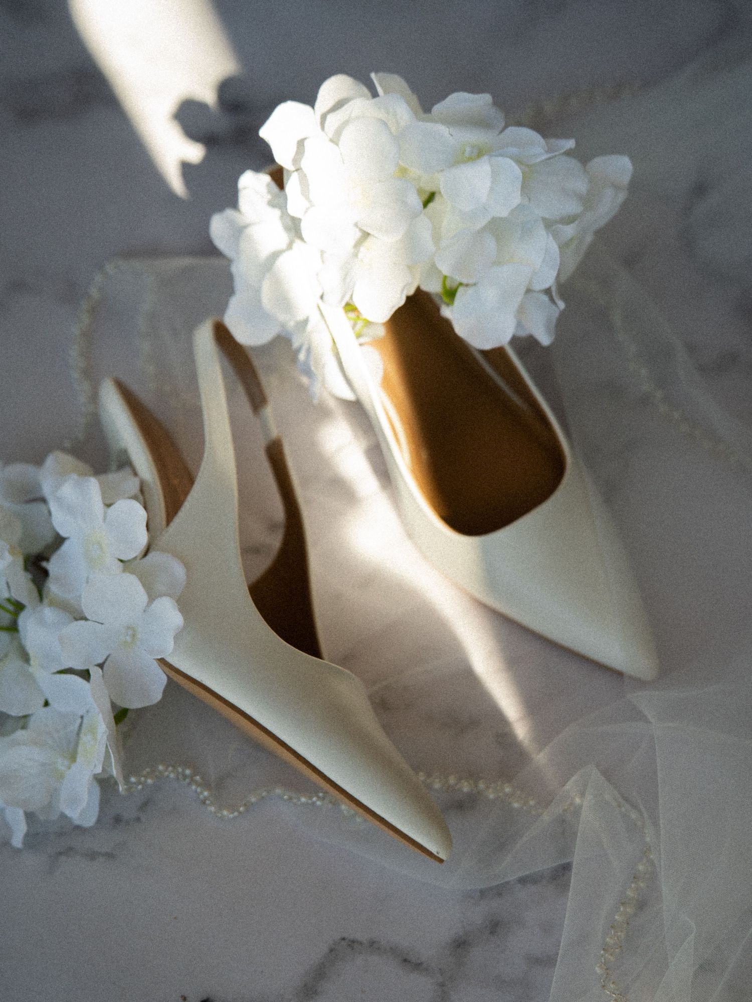 Elegant ivory bridal heels with white hydrangea flowers and pearl details on marble surface.