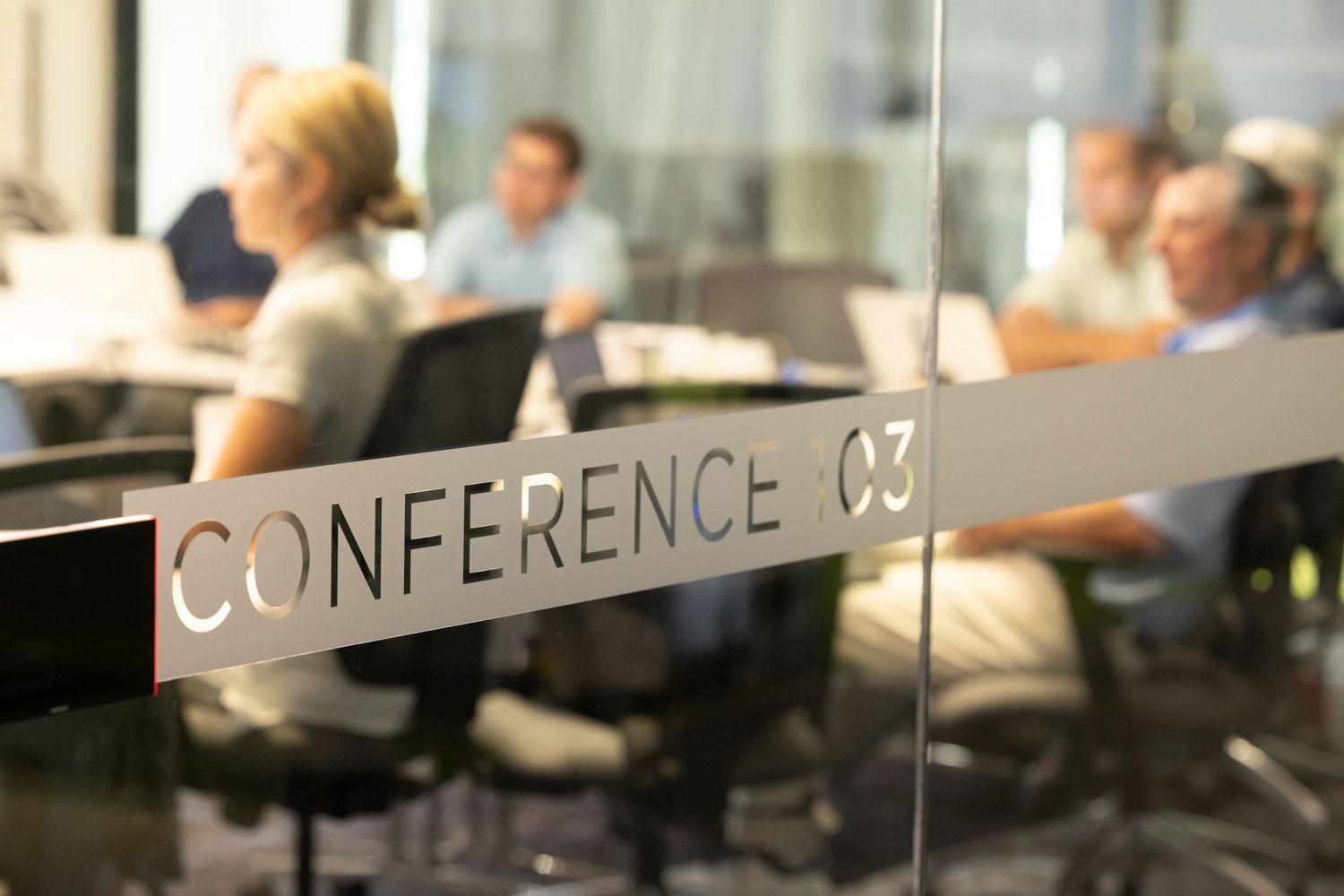 Glass door sign reading Conference 03 with blurred business professionals meeting in a modern office conference room.