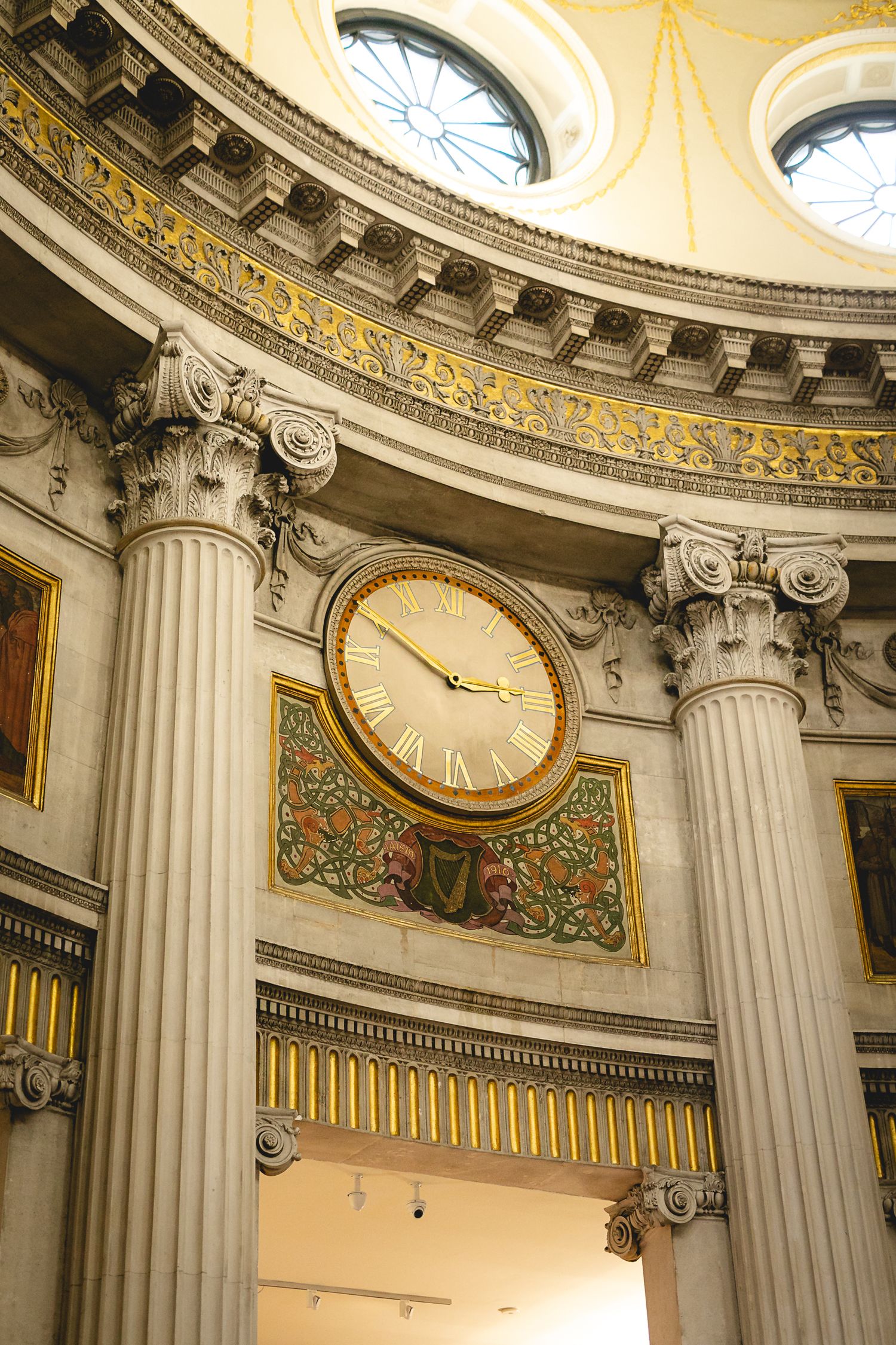 Ornate neoclassical rotunda interior featuring tall Corinthian columns, decorative clock with Roman numerals, and gilded dome ceiling.