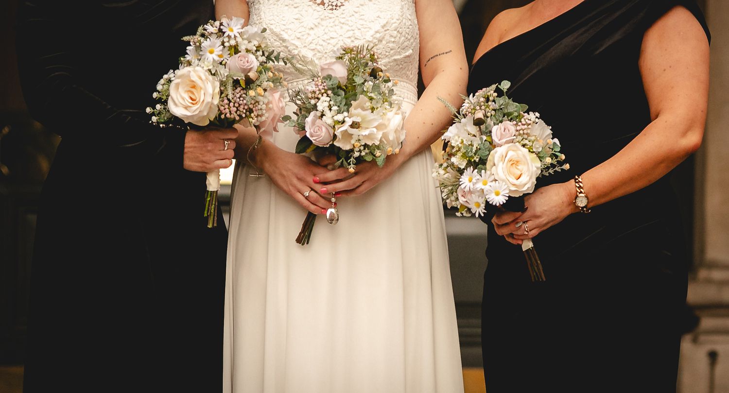 Bride and bridesmaid holding elegant white rose and baby's breath bouquets at a wedding ceremony.