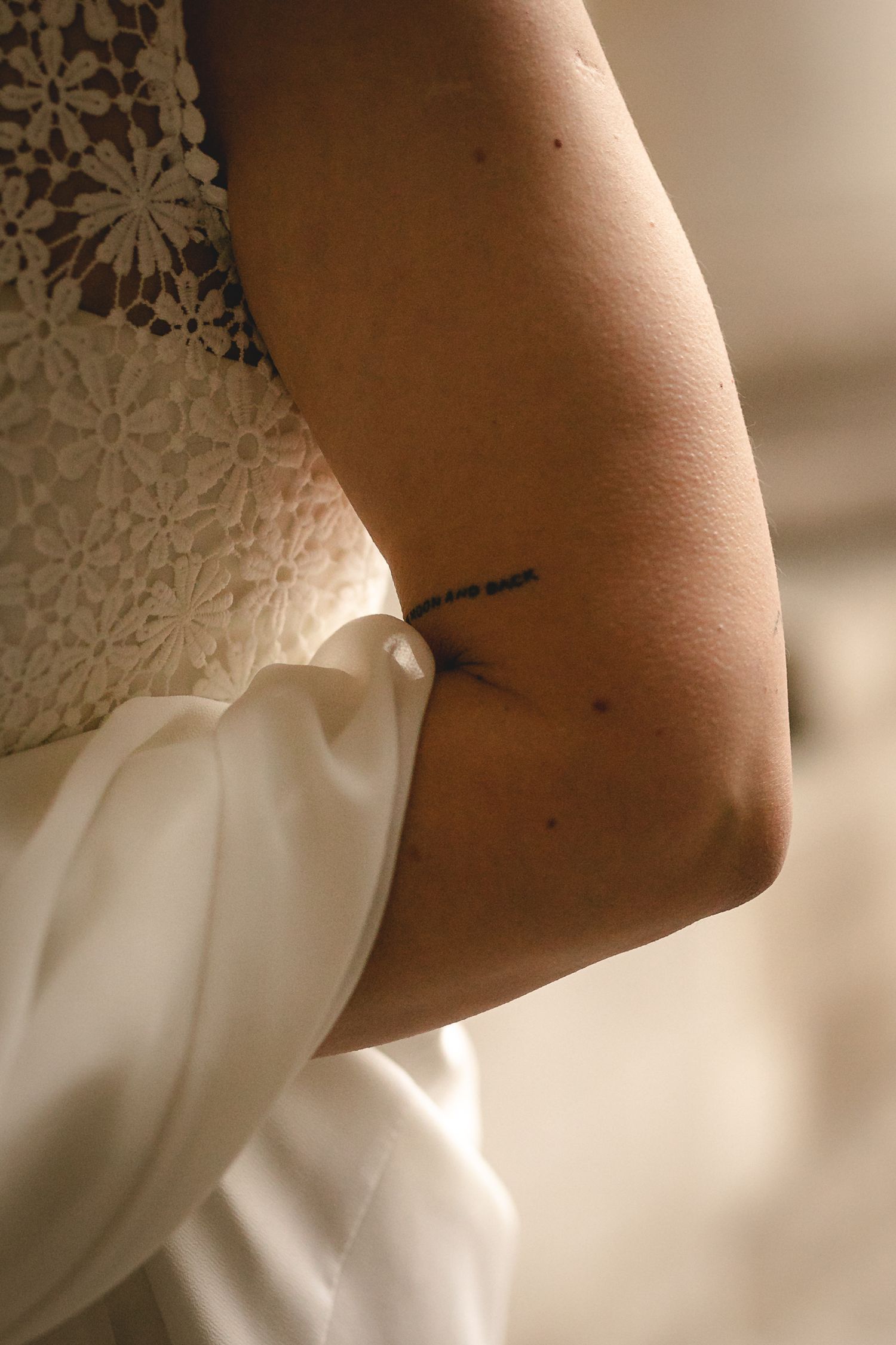 Close-up of a bride's arm showing a small delicate tattoo while wearing a white lace wedding dress.