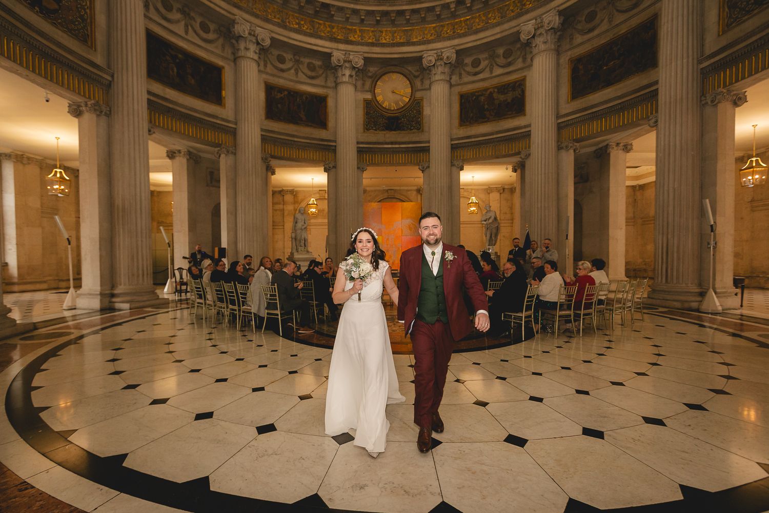 Newlyweds walk down aisle in stunning domed rotunda after wedding ceremony.