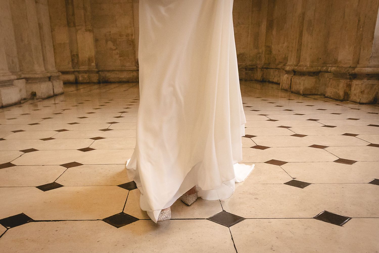 Bottom of a white wedding dress train on a black and white checkered marble floor.